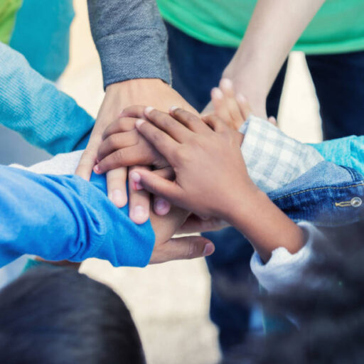 In this closeup with only hands showing, a group of volunteer workers, adults and children, stand outside and stack their hands together in celebration of a job well done.